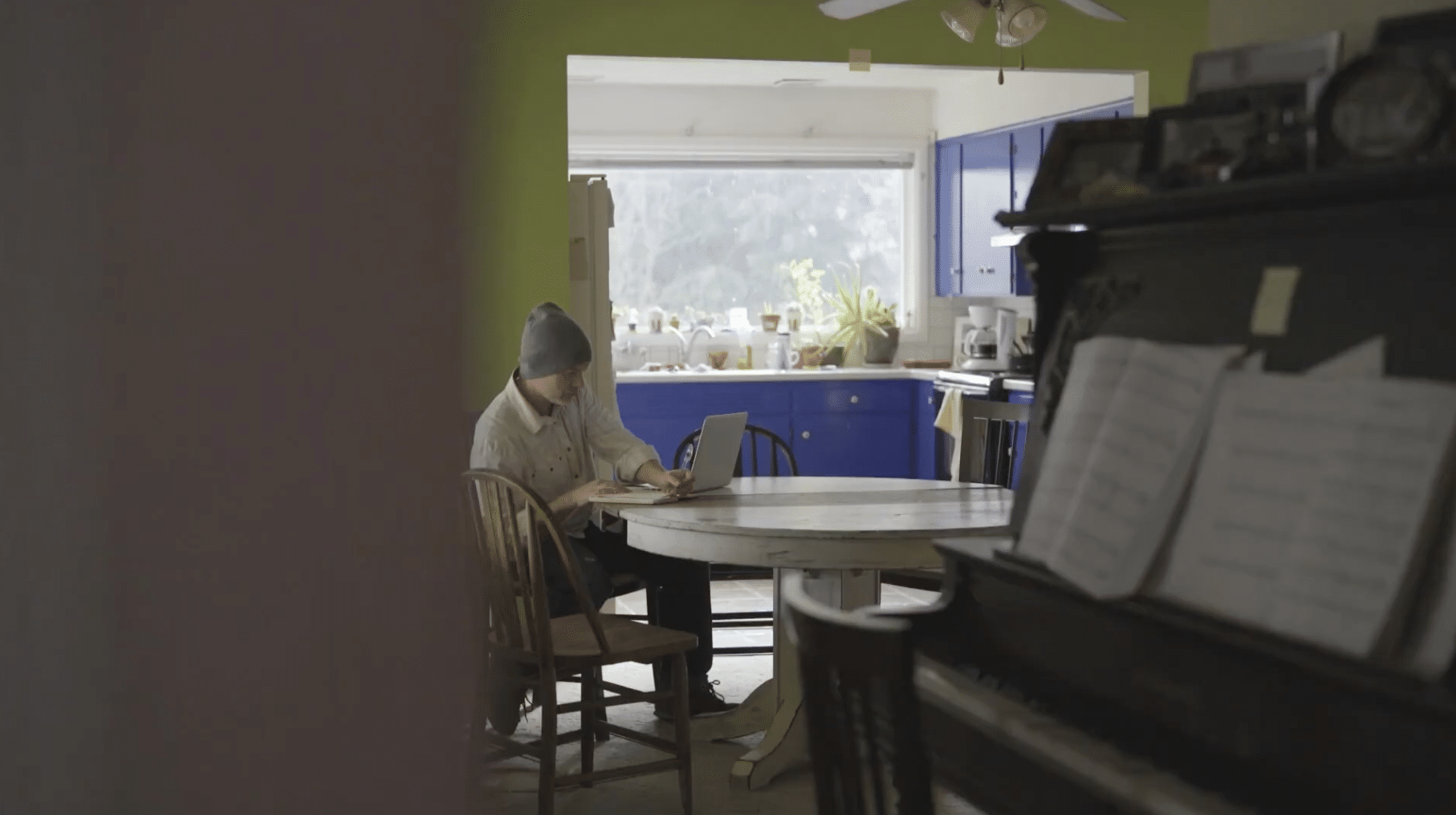 Person sitting at kitchen table, writing on note pad while looking at a laptop