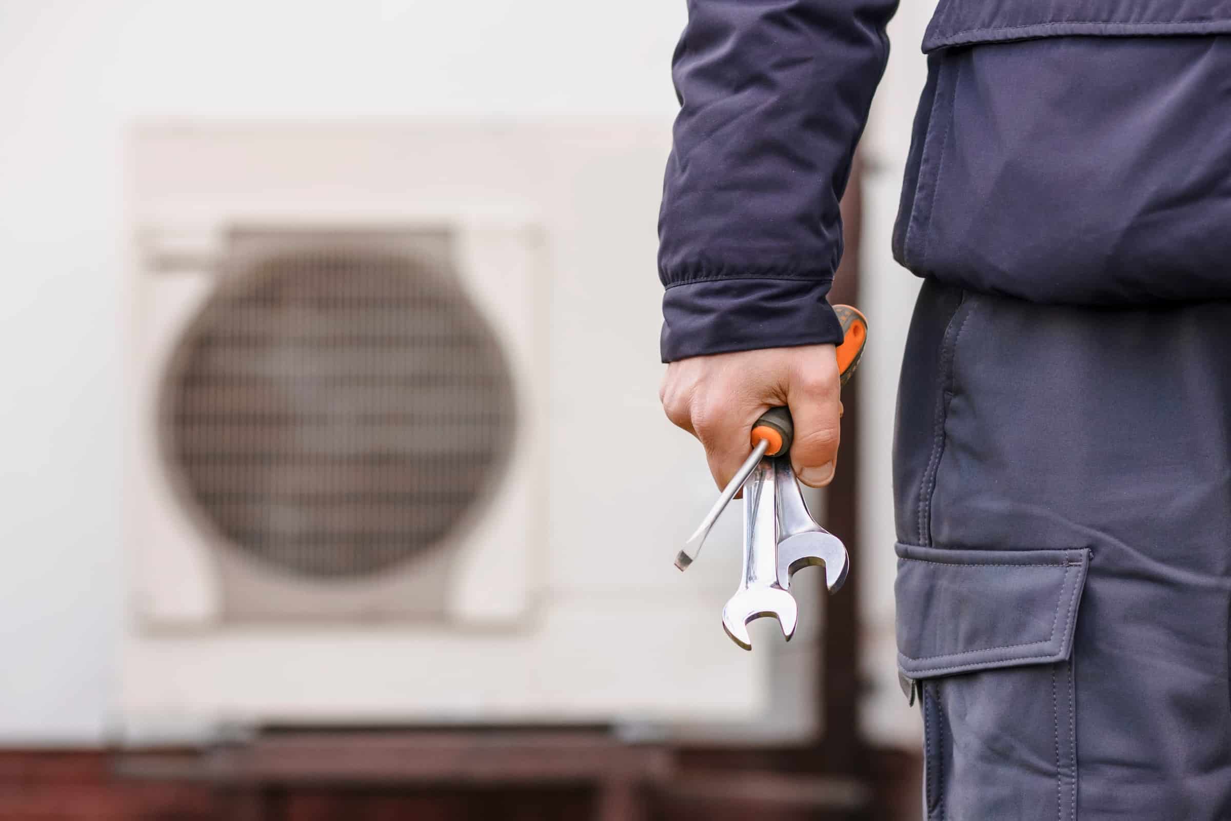 Hand holding tools in front of installed heat pump